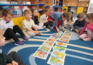 Chłopiec układa obrazki, pozostałe dzieci siedzą wokół niego.