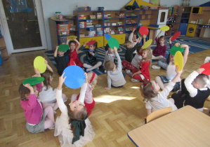 Dzieci siedzą na dywanie, trzymają w rękach krążki gimnastyczne.