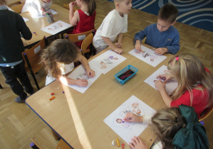 Dzieci siedzą przy stolikach i wyklejają plasteliną obrazki z postaciami z bajek.