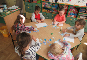 Dzieci siedzą przy stoliku i wykonują prace plastyczne.