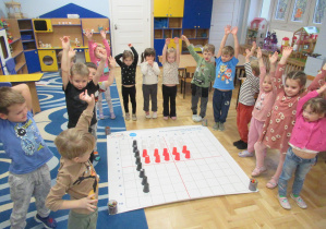 Dzieci stoją wokół maty do kodowania, na macie ułożona flaga Polski z kubeczków.