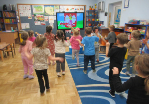 Dzieci tańczą, przed nimi ekran multimedialny, na którym godło i flada Polski.
