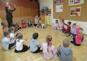 Dzieci siedzą w kole podczas rytmiki, dzieci grają na instrumentach.