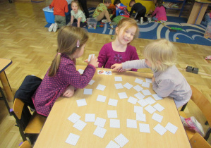 Dziewczynki siedzą przy stoliku i grają w memory.