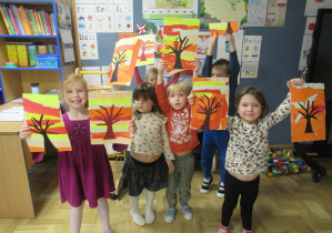 Dzieci trzymają w rękach prace plastyczne - jesienne drzewa.