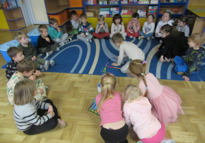 Dzieci siedzą w kole, chłopiec układa figurę z kredek ołówkowych.