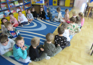 Dzieci siedzą w kole na dywanie.