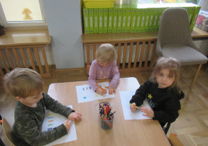 Dzieci wykonują karty pracy przy stoliku.