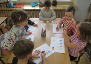 Dzieci siedzą przy stoliku i wykonują karty pracy.