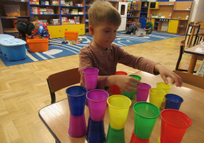 Chłopiec przy stoliku układa kolorowe kubeczki.