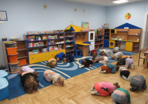 Dzieci w sali przedszkolnej w pozycji klęczącej skulonej udają śpiące niedźwiadki.