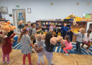 Dzieci przytulają lub podrzucają swoje pluszowe misie.