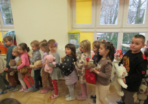 Dzieci stoją w rzędzie, trzymają w rękach pluszowe misie.