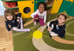 Dziewczynki siedzą przy słońcu ułożonym z papierowego koła i kredek