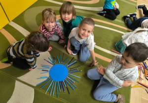 Dzieci siedzą przy słońcu ułożonym z papierowego koła i kredek