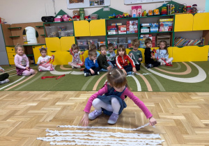 Dziewczynka kładzie na podłodze biały pasek wycięty z krepiny