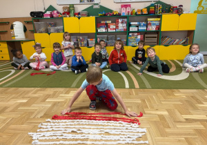 Chłopiec kładzie na podłodze czerwony pasek wycięty z krepiny