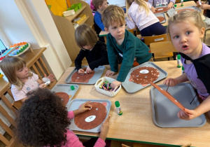 Dzieci przyklejają elementy misowych pyszczków do papierowych talerzy
