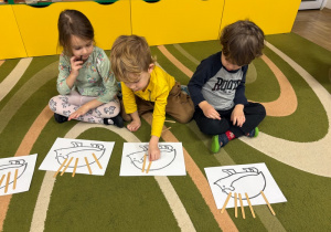 Dzieci układają kolce z drewnianych patyczków na sylwetach przedstawiających jeże