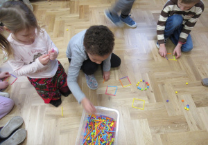 Dzieci na podłodze układają figury geometryczne z patyczków.