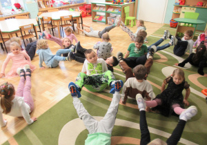 Dzieci ćwiczą w parach, dotykają się podeszwami stóp.