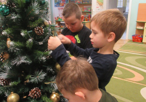 Chłopcy wieszają bombki na choince.