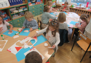 Dzieci przy stolikach wykonują prace plastyczne.