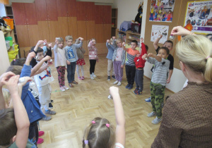 Dzieci stoją w kole podczas zajęć rytmiki, w ręku trzymają dzwoneczki.
