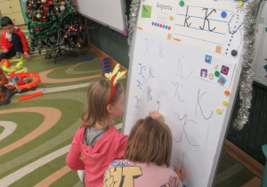Dziewczynki piszą literki na tablicy.