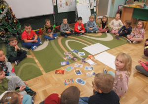 Dzieci siedzą w kole, przed nimi kartki świąteczne.