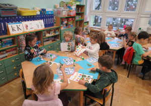 Dzieci siedzą przy stolikach i wykonują prace plastyczne.