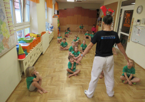 Dzieci siedzą na podłodze podczas zajęć taekwondo.