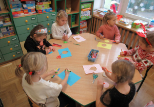 Dziewczynki przy stoliku wykonują prace plastyczne.