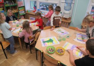 Dzieci przy stolikach malują farbami.