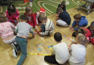 Dzieci układają na podłodze choinkę z klocków.