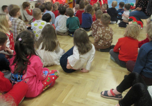 Dzieci siedzą na podłodze, przed nimi Święty Mikołaj.