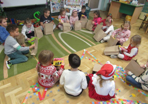 Dzieci siedzą w kole i oglądają prezenty od Świętego Mikołaja.