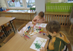 Dzieci malują farbami drewniane choinki.