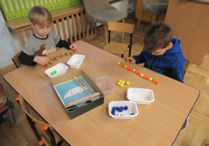 Chłopcy siedzą przy stoliku i układają kolorowe pomponiki.