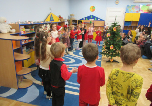 Dzieci stoją w półkolu podczas występu świątecznego dla rodziców.