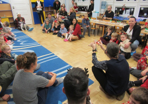 Dzieci i rodzice siedzą na podłodze podczas warsztatów.