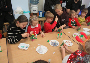 Dzieci z rodzicami ozdabiają choinki.