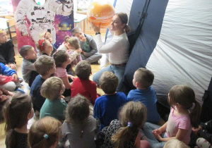 Dzieci siedzą przed planetarium rozstawionym w sali.