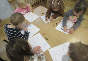 Dzieci siedzą przy stoliku i wykonują matematyczne karty pracy