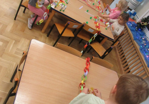 Dzieci przy stolikach wykonują łańcuchy z papieru.