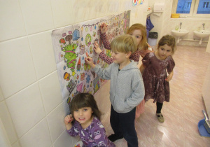 Dzieci kolorują kolorowankę powieszoną na ścianie.