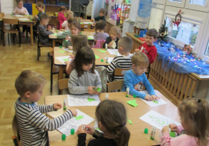 Dzieci siedzą przy stolikach i wykonują prace plastyczne.