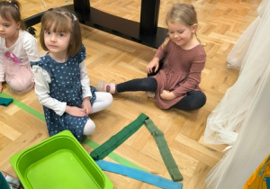 Dziewczynki siedzą obok trójkąta ułożonego z szarf