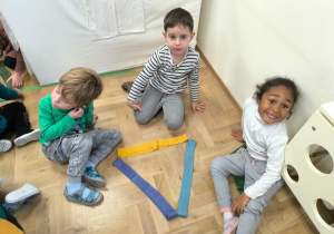 Dzieci siedzą obok trójkąta ułożonego z szarf