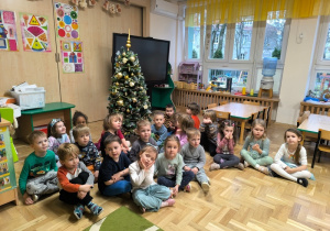 Dzieci siedzą przed choinką